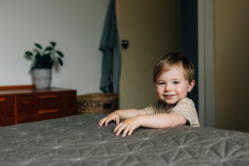 Boy smiling at camera, standing next to bed