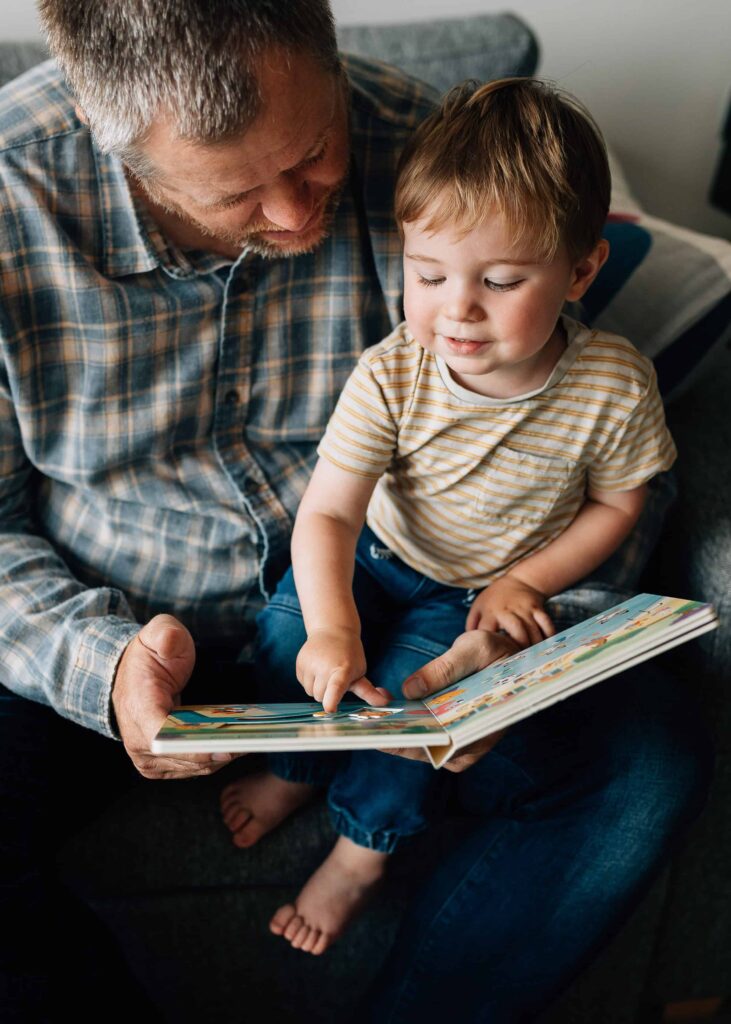 Son on Dad's knee as they read a board book, value of photography, especially plus size family photos