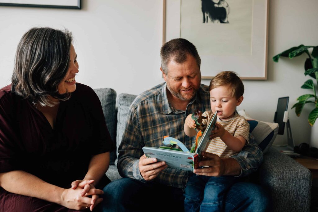 Boy shows dad a book, sitting on couch, value of photography, especially plus size family photos